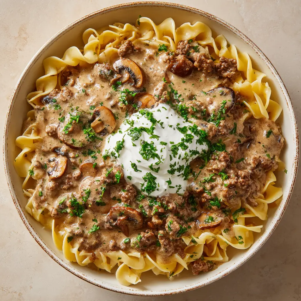 Close up view of the thick light brown gravy with browned ground beef crumbles and tender sliced cremini mushrooms.