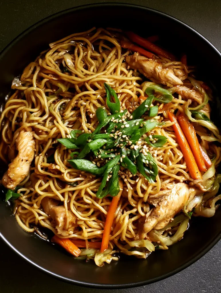 Close-up of glossy thin yellow egg noodles coated in dark brown sauce. (Chicken Chow Mein Recipe)