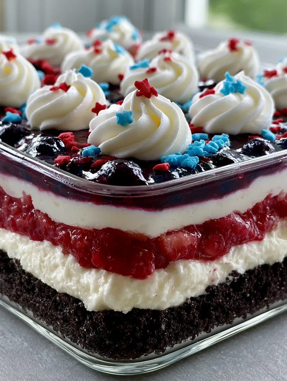 Patriotic Dessert Lasagna: The Ultimate Red, White, and Blue Layered No-Bake Treat 3 A close-up photo of the Patriotic Dessert Lasagna in a glass dish with whipped cream swirls and star sprinkles on top.