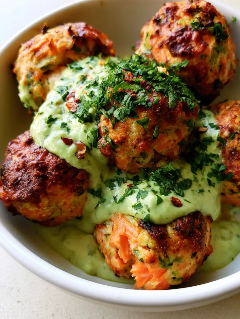 Top-down view of charred Baked Salmon Meatballs with visible pink flakes and green herbs in a white ceramic bowl.