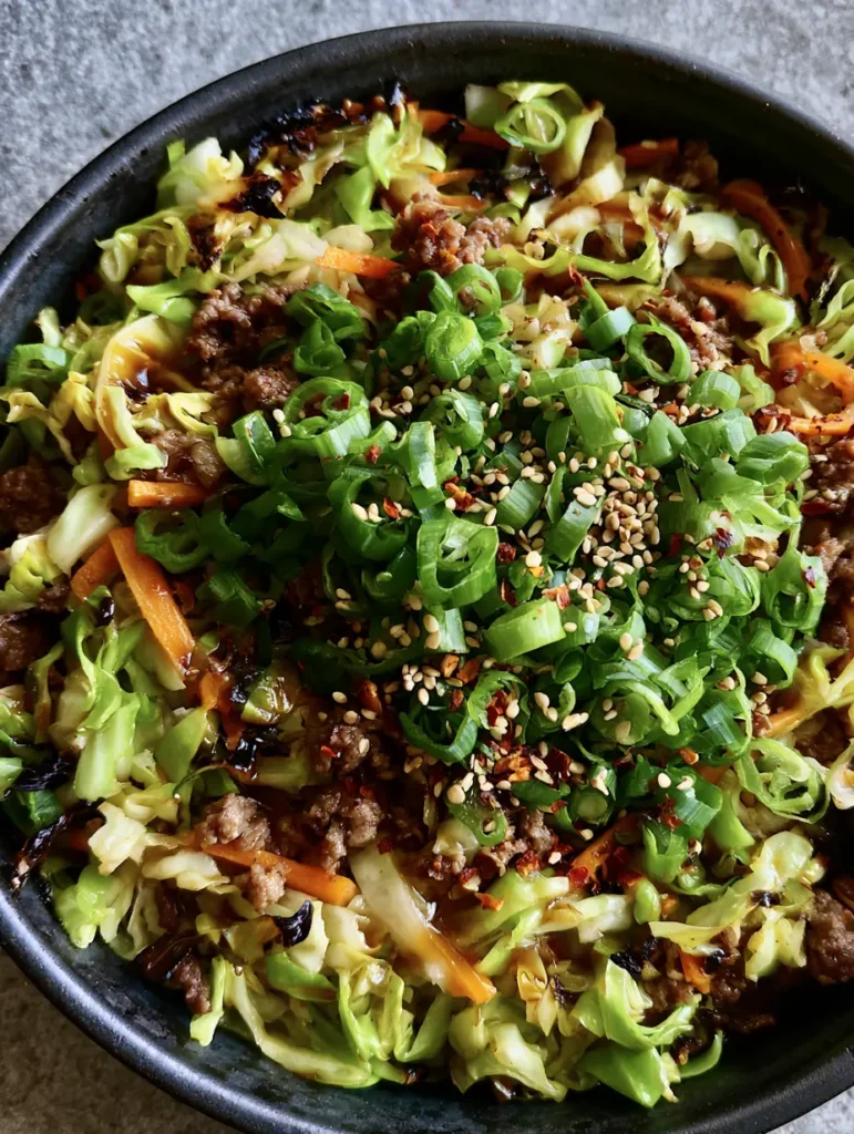 Ginger Ground Beef Stir Fry in a rustic black ceramic bowl topped with heavy sesame seeds and red chili flakes.