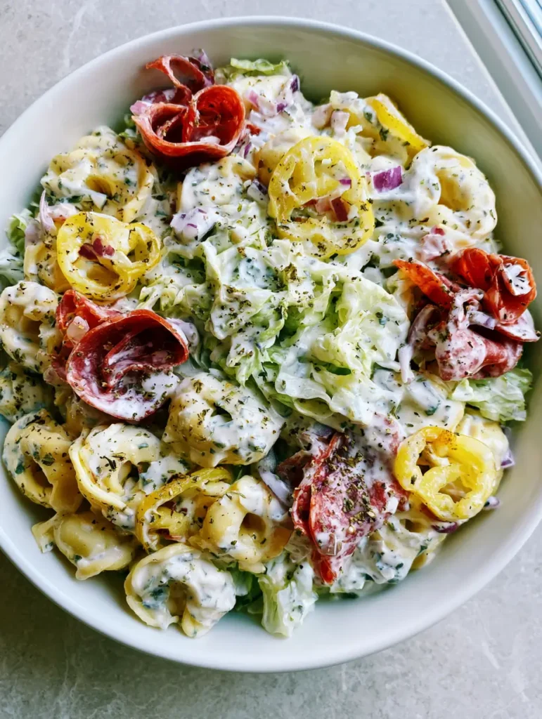 Italian Grinder Tortellini Salad: The Ultimate Viral Creamy Pasta Mashup 1 Italian Grinder Tortellini Salad served in a white ceramic bowl on a gray stone countertop.