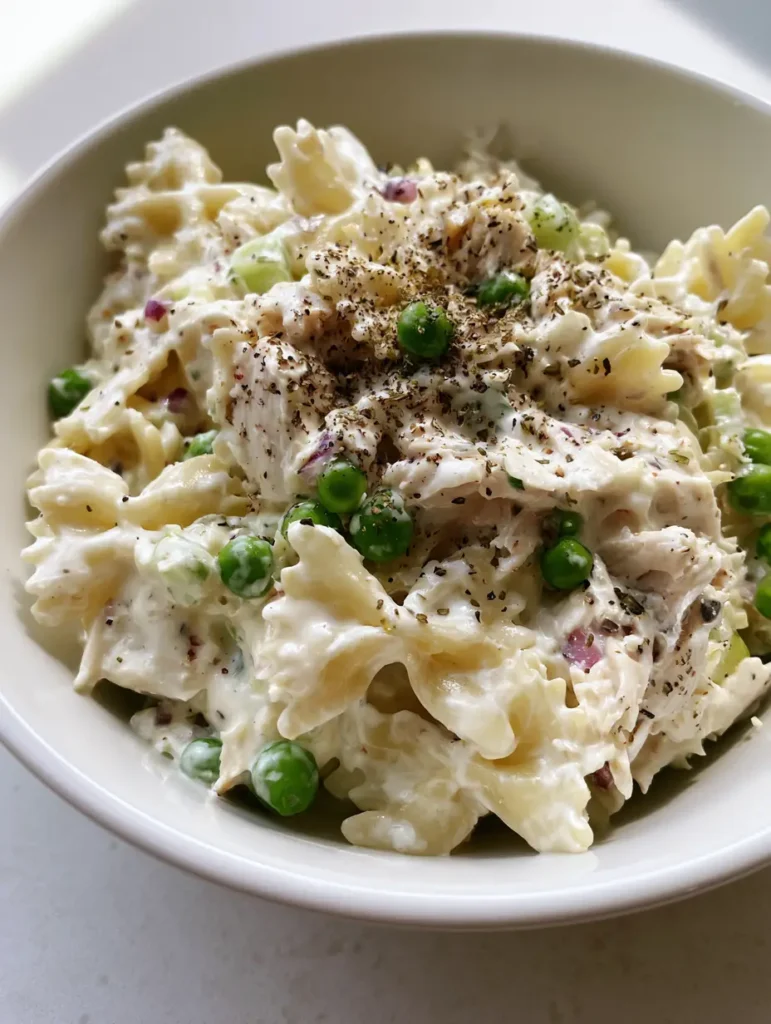 Close-up detail of bowtie pasta coated in a thick, opaque creamy dressing with cracked black pepper. (Creamy Chicken Pasta Salad)