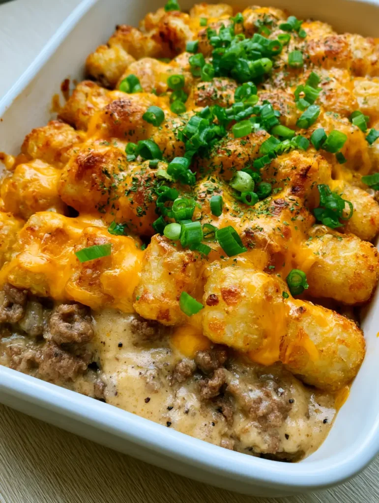 Tater Tot Casserole with Crispy Golden Tots and Sharp Melted Cheddar 1 Handheld photo of a ceramic dish filled with Tater Tot Casserole featuring a creamy beef base and crispy potatoes.
