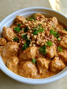 Overhead shot of Slow Cooker Peanut Chicken showing the thick orange-brown sauce and tiny spice flecks.