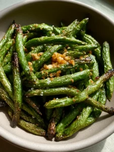 Top-down view of charred Air Fryer Green Beans with visible sea salt flakes and olive oil sheen.