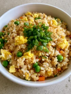 Close-up handheld smartphone photo of Egg Fried Rice in a white bowl showing distinct grains with a light golden-brown soy sauce tint.