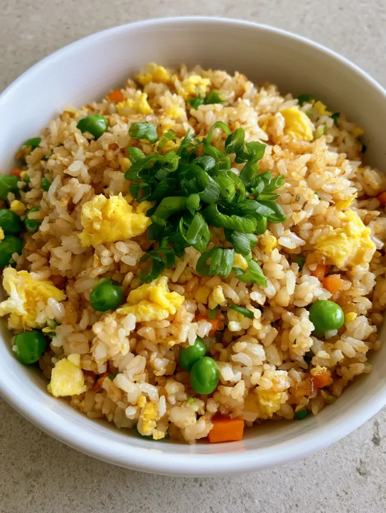 Egg Fried Rice: The Secret to Fluffy, Restaurant-Style Grains at Home 2 Close-up handheld smartphone photo of Egg Fried Rice in a white bowl showing distinct grains with a light golden-brown soy sauce tint.
