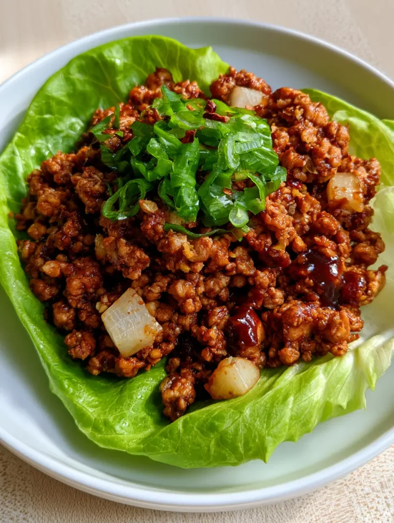 A handheld smartphone photo of a fresh chicken lettuce wrap sitting on a ceramic plate. (Chicken Lettuce Wraps)