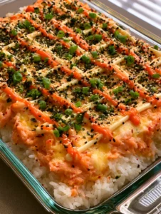 Top view of a creamy salmon sushi bake showing the bubbly seafood topping and vibrant sriracha mayo lines. (Salmon Sushi Bake)