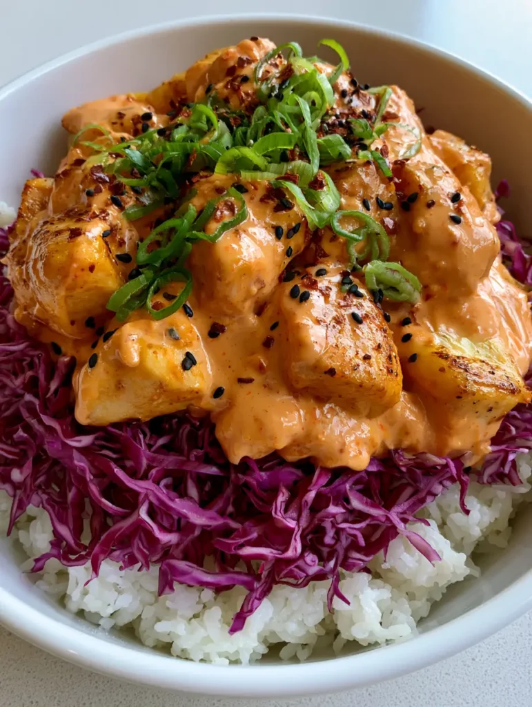 Close-up of seared chicken breast in a Bang Bang Chicken Bowl garnished with sliced green scallions, black sesame seeds, and red chili flakes.