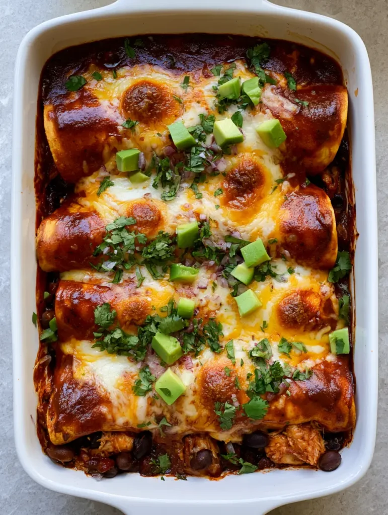 High Protein Chicken Enchiladas: The Ultimate Cheesy Shredded Thigh and Bean Bake 1 A top-down view of the ceramic baking dish showing shredded chicken and black beans visible at the ends of the rolls. (High Protein Chicken Enchiladas)