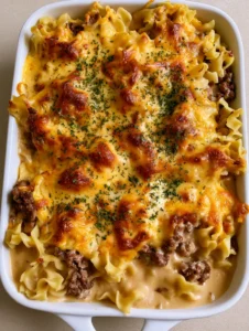 High-angle view of Amish Hamburger Casserole showing wavy noodles and creamy beige sauce topped with melted cheddar.