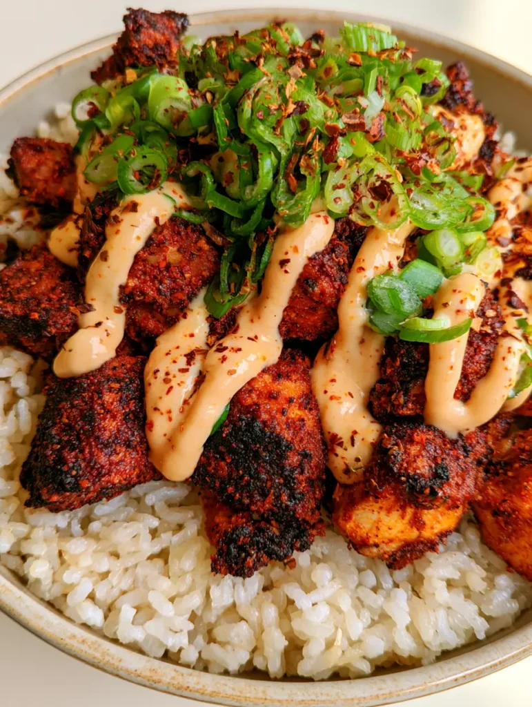 Crispy Cajun Chicken Rice Bowl with Creamy Spicy Mayo 1 Crispy Cajun Chicken Rice Bowl in a shallow ceramic dish garnished with scallions and chili flakes.